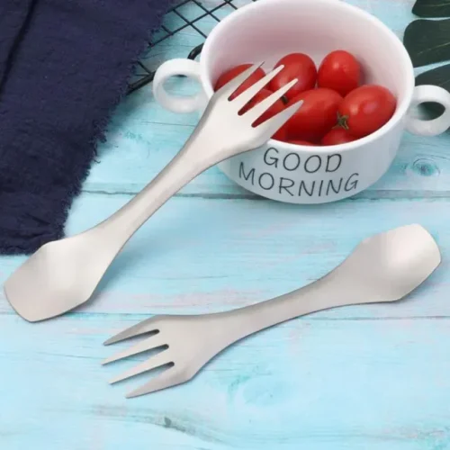 Zwei Titan-Sporks neben einer Schale mit Tomaten auf einem hellblauen Holztisch