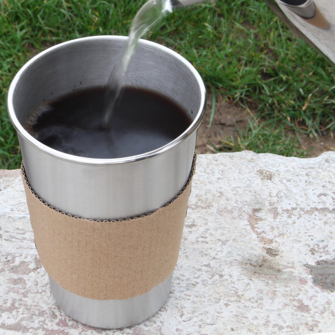 Kaffee wird in einen Edelstahlbecher mit Becherhülle aus Kraftpapier gegossen