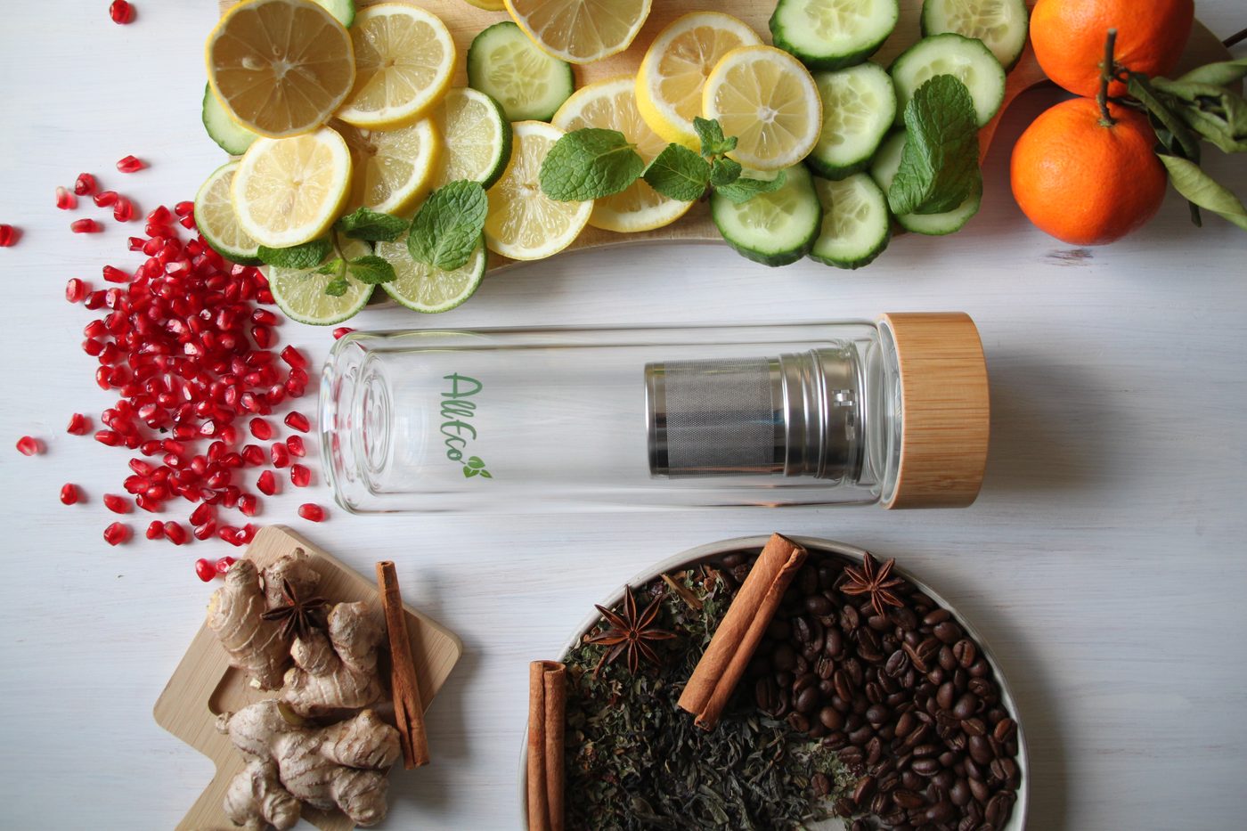 Teebereiter aus doppelwandigem Glas mit Edelstahlsieb zwischen Zitronen, Gurken, Granatapfel und Tee
