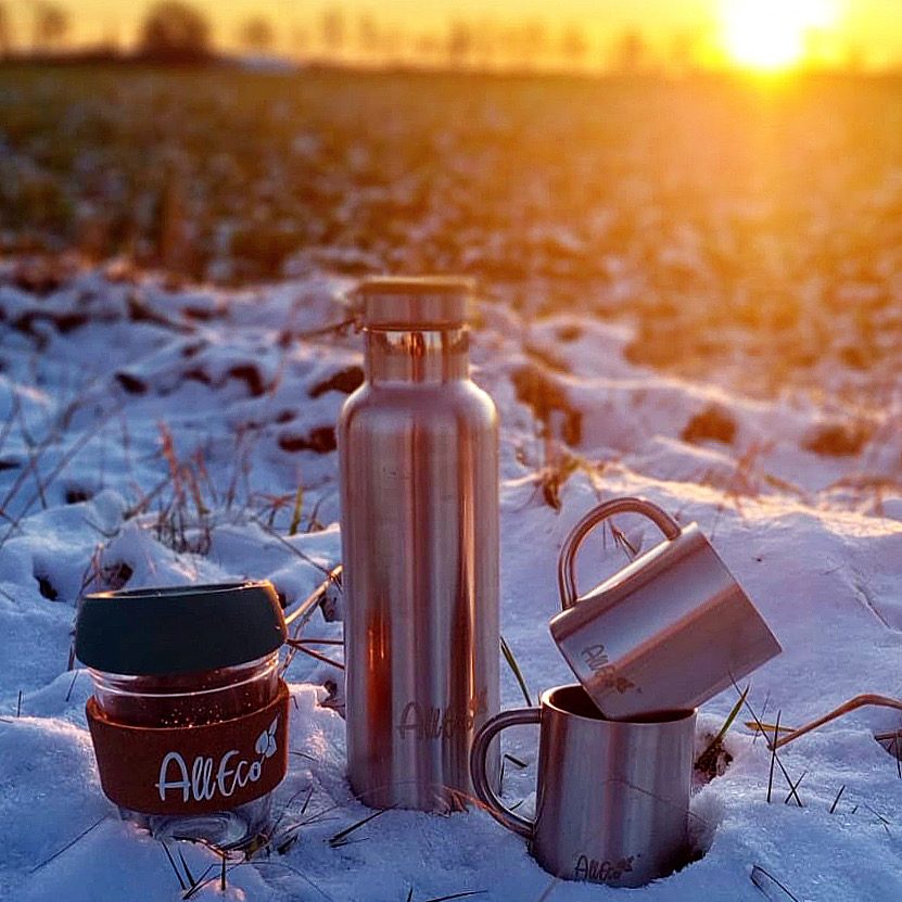 Edelstahl-Trinkflasche, Thermobecher und Kaffeebecher aus Glas im Schnee bei Sonnenuntergang
